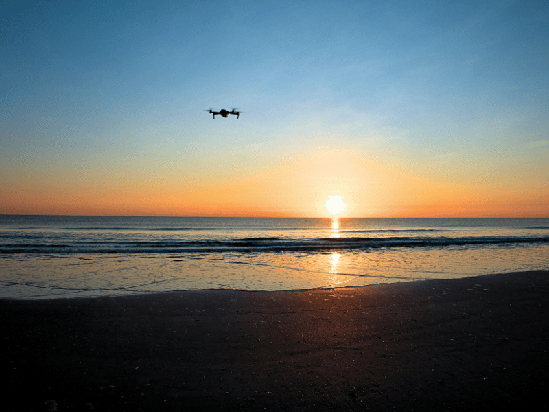 Drone flying over water on a beach with the sun on the horizon