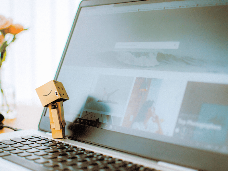 Amazon boxes robot looking at a laptop screen for news on the first Amazon drone delivery