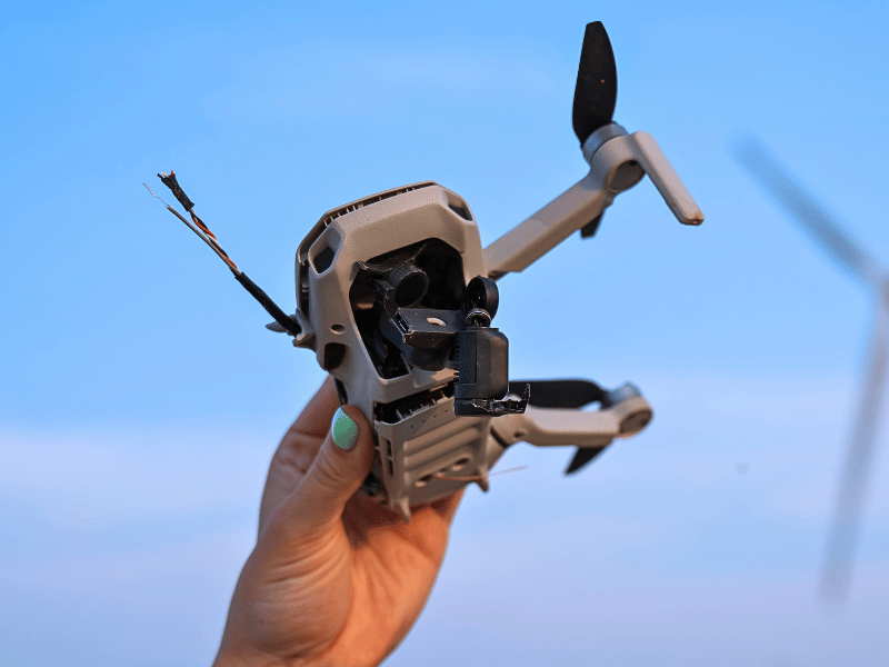Damaged drone being held up by a person in front of a blue sky
