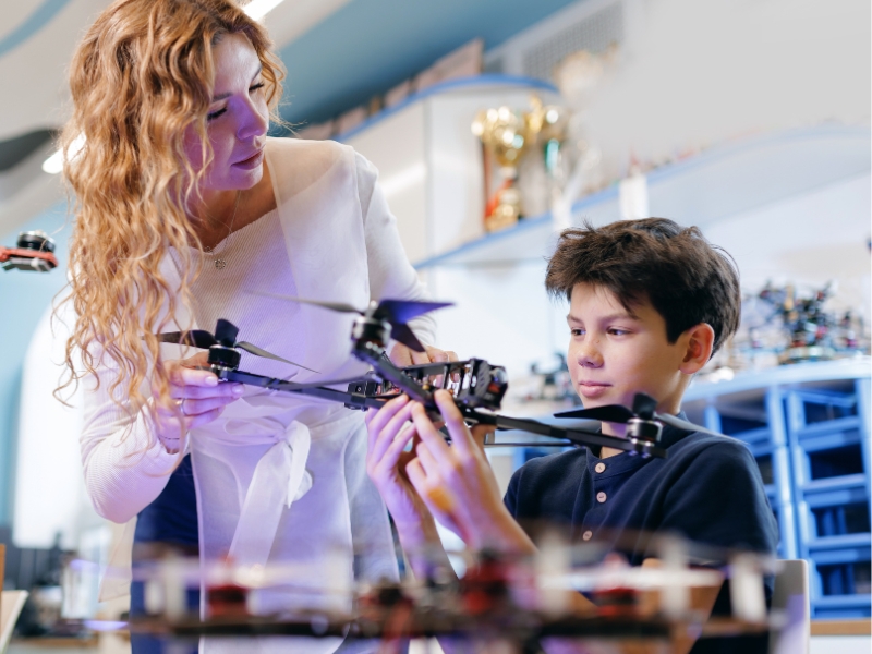 A teacher and a young student in a classroom, working together on a drone project.