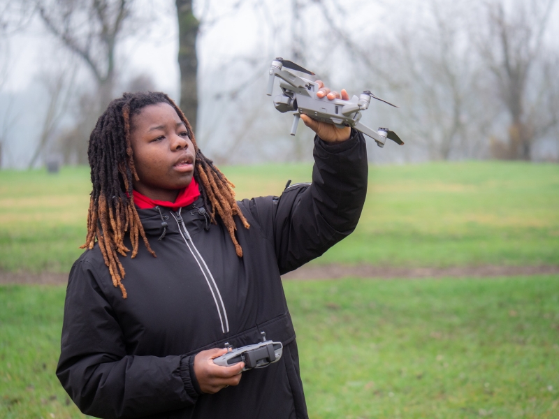 A child in a field holding and inspecting a drone.